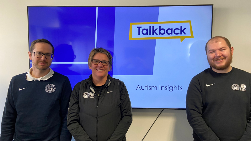 Alastair Kay, Liz Verrall and Hans Cook from Berks & Bucks FA stand in front of a screen displaying the Talkback logo